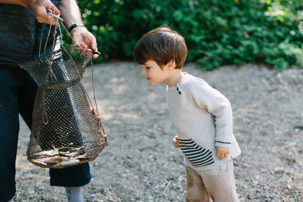 Petit garçon qui rencontre un pêcheur et est curieux des poissons pêchés