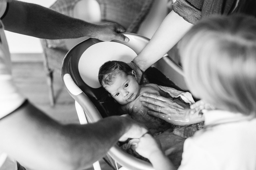 Photographie en noir et blanc d'un bébé dans le bain avec les mains de maman sur lui