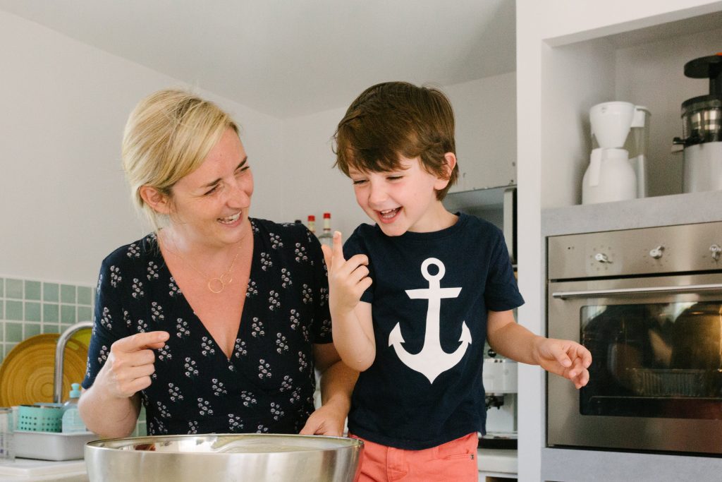 Photo d'un enfant qui se lèche les doigts dans une cuisine en train de pâtissier avec sa maman