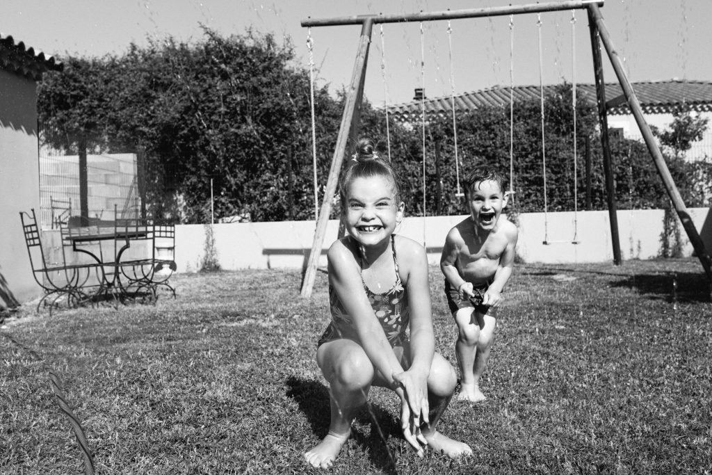 Photographie en noir et blanc de deux enfants qui jouent dans leur jardin en plein été
