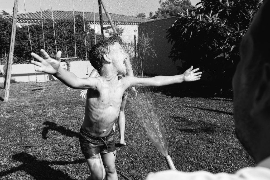 Photographie en noir et blanc d'un enfant jouant devant un jet d'eau
