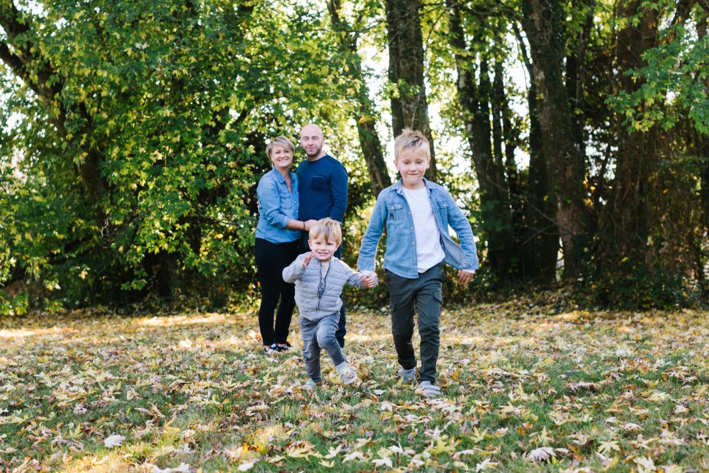 Photographie de deux enfants qui courent avec leurs deux parents en arrière plan