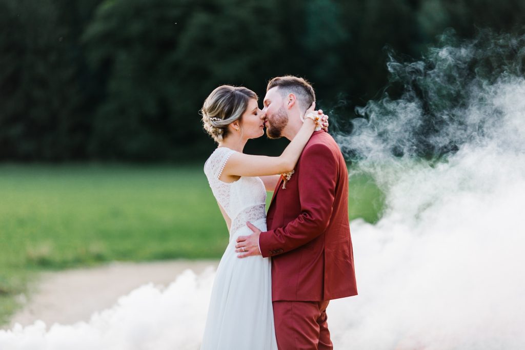 Bisou de mariés avec des fumigènes en arrière plan de la photo